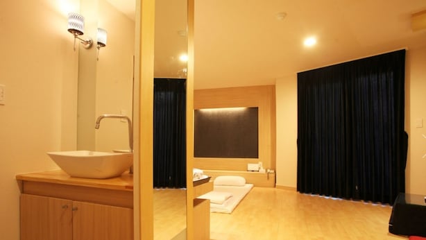 Un baño moderno con un lavamanos grande, un armario de madera y un espejo. Hay una zona de ducha con cortina y una toalla en el suelo.