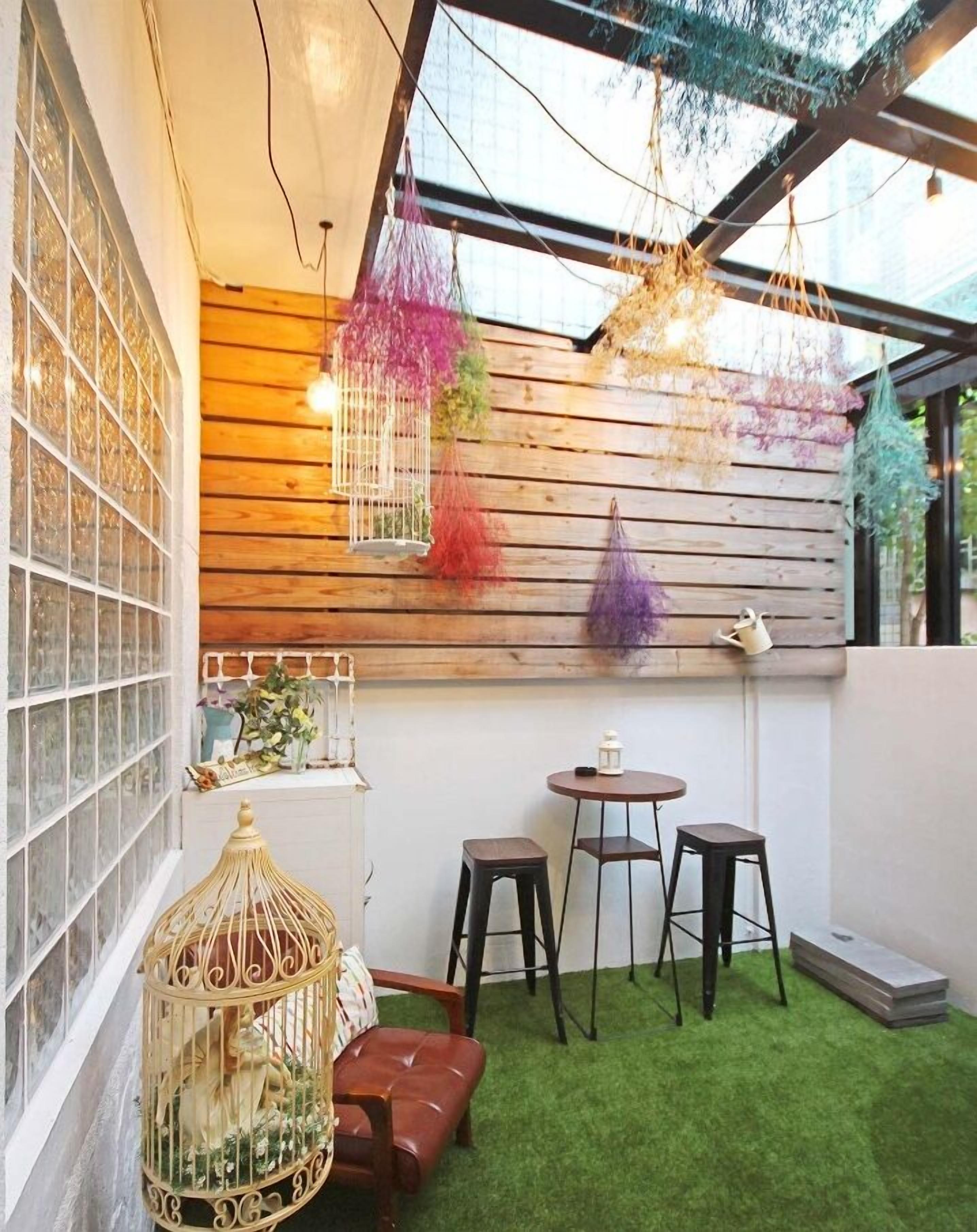 Un espacio al aire libre acogedor con pared de madera, una mesa pequeña, dos taburetes y una jaula de pájaros.