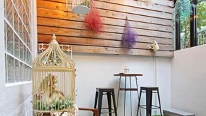 Una habitación con techo de listones de madera, suelo de césped artificial verde, una jaula decorativa y dos taburetes negros.