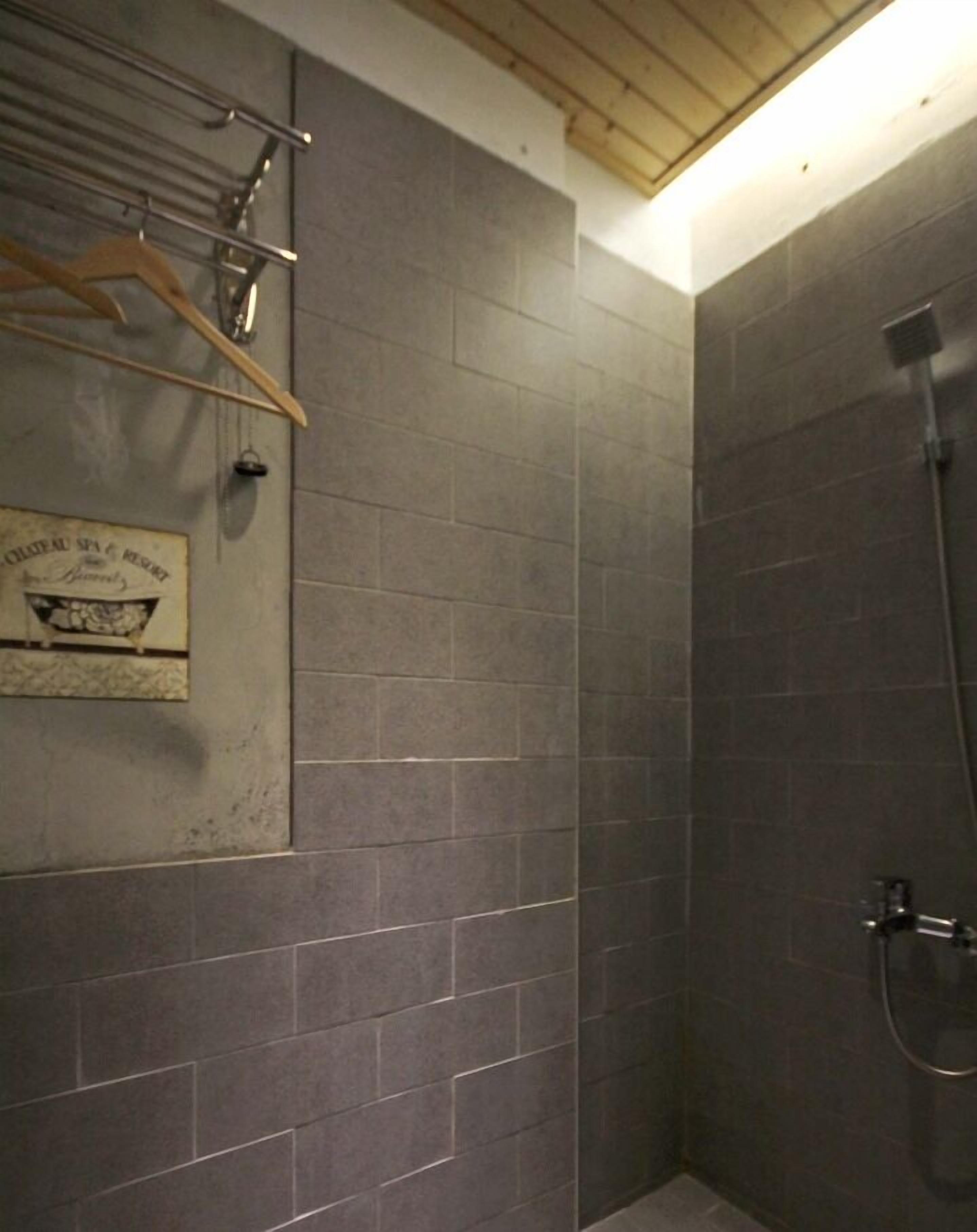 Un baño con baldosas gris oscuro, techo de madera y zona de ducha.