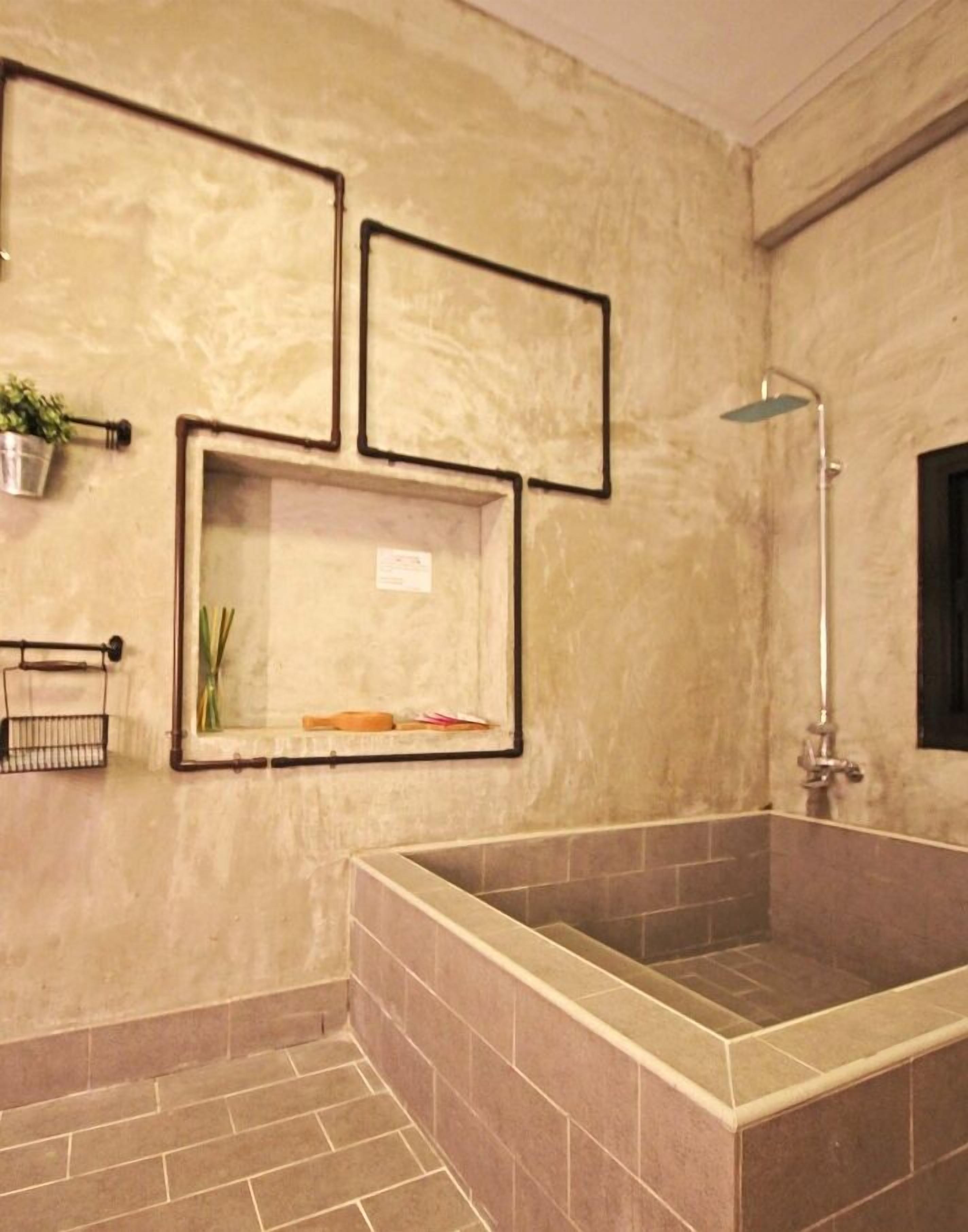 Une salle de bain dotée d’une grande baignoire, de murs carrelés et d’une étagère murale agrémentée d’une plante et de produits de toilette.