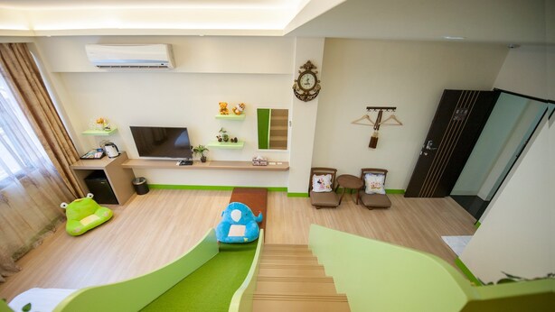 Una sala de estar moderna con un televisor de pantalla plana, estanterías verdes, un sofá, una mesita y una escalera.