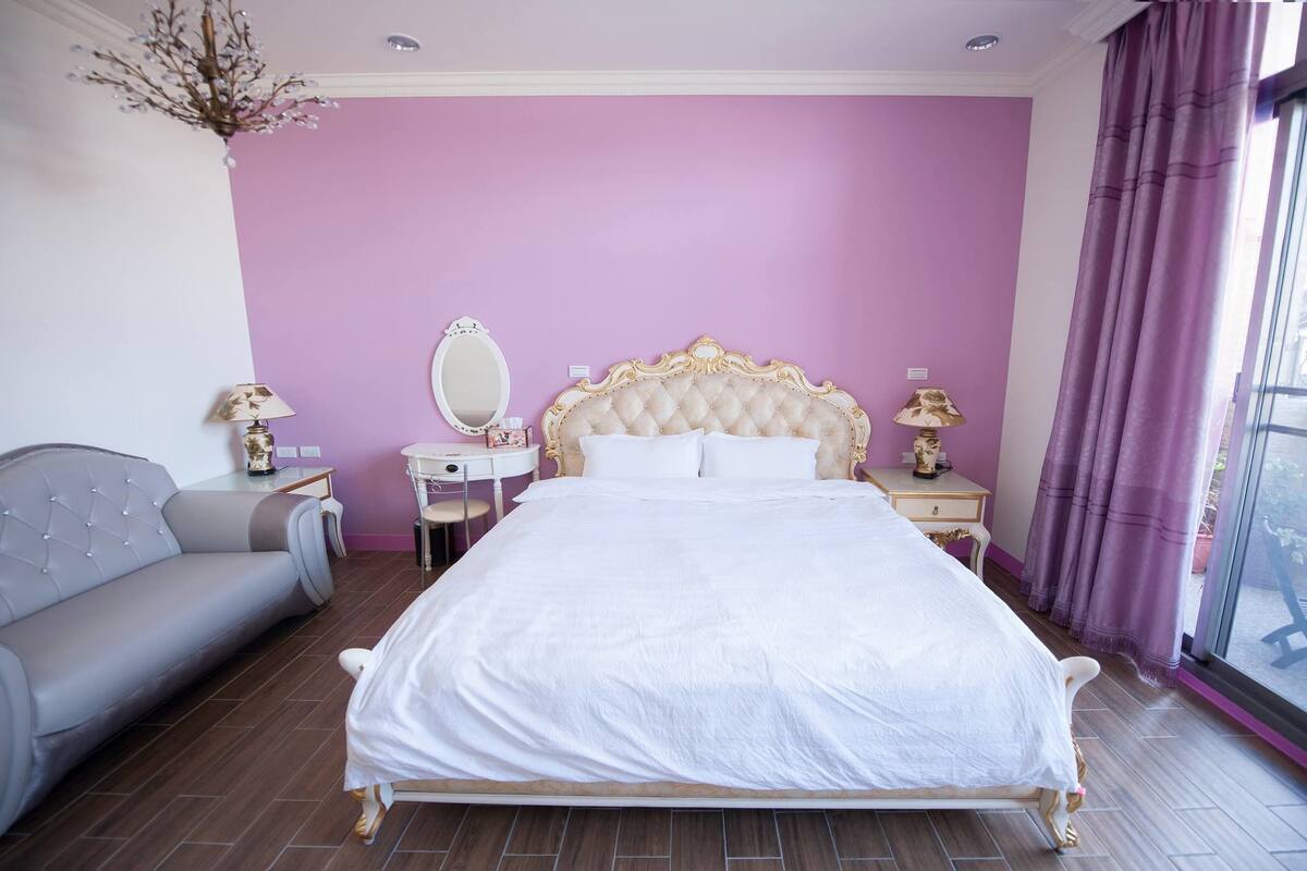 Ein Schlafzimmer mit einem großen Bett, einem Schminktisch mit Spiegel, einem Sofa und einer Kandelaber.