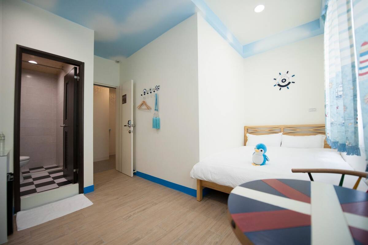 Ein Hotelzimmer mit Schachbrettmuster-Boden, einem Bett mit einer Pinguin-Dekoration, einer Wanduhr und einem Kleiderhaken mit Kleiderbügeln.