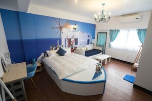 A modern bedroom with a curved bed, a desk, and a chair. There is a large window with curtains, a chandelier, and a wall mural.