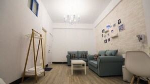 Una habitación con piso de madera, un sofá blanco, una pequeña mesa, un perchero y un candelabro.