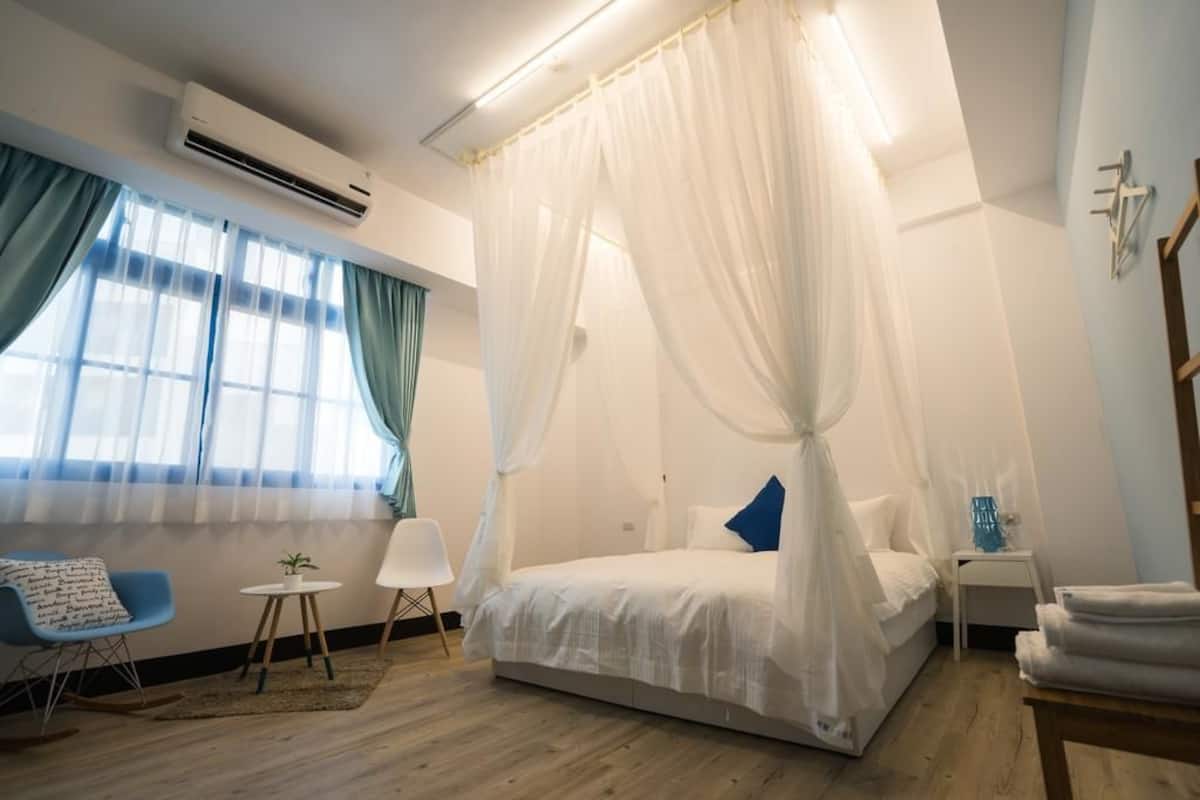 A bedroom with a canopy bed, a bedside table, a chair, and a small table with a plant.