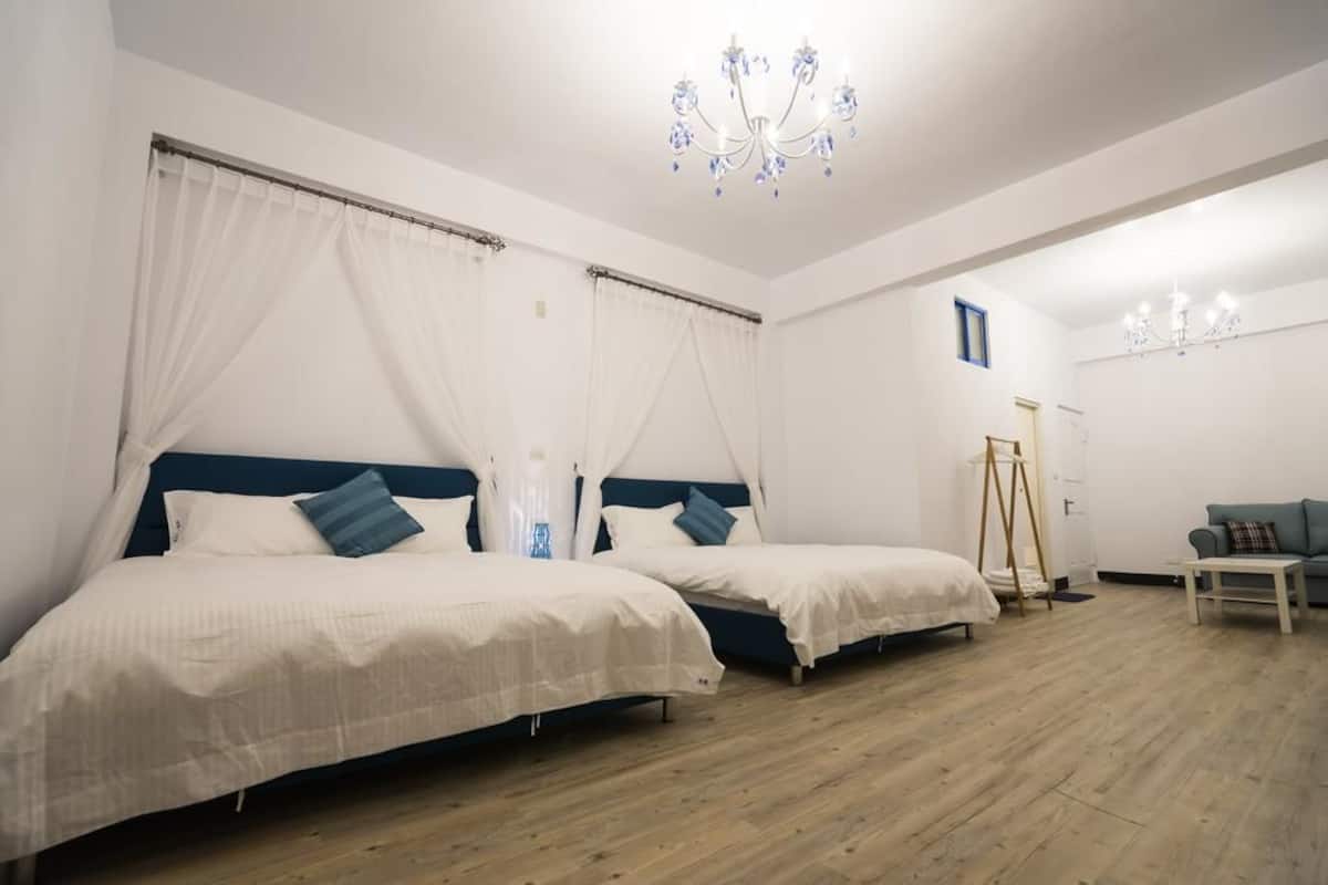 A bedroom with two beds, a standing lamp, and a small table.