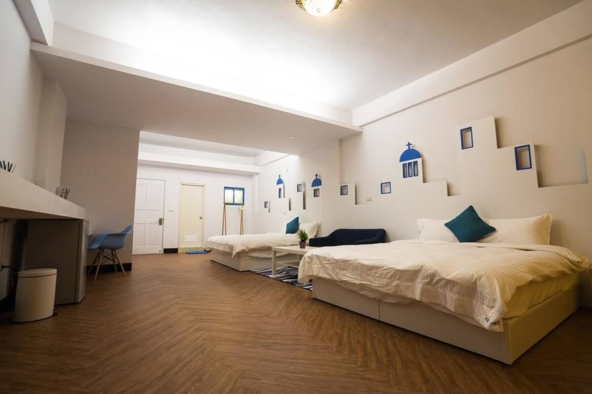 A modern hotel room with a wooden floor, two beds, a desk, and a chair.