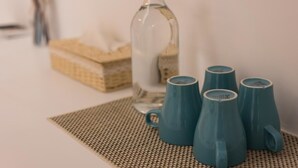 Una botella de vidrio transparente y cuatro tazas azul verdoso sobre un camino de mesa tejido.