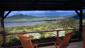 A balcony with two wooden chairs overlooking a scenic view of a lake and mountains. - La Hacienda Old Grand Port Mauritius (Vieux Grand Port)