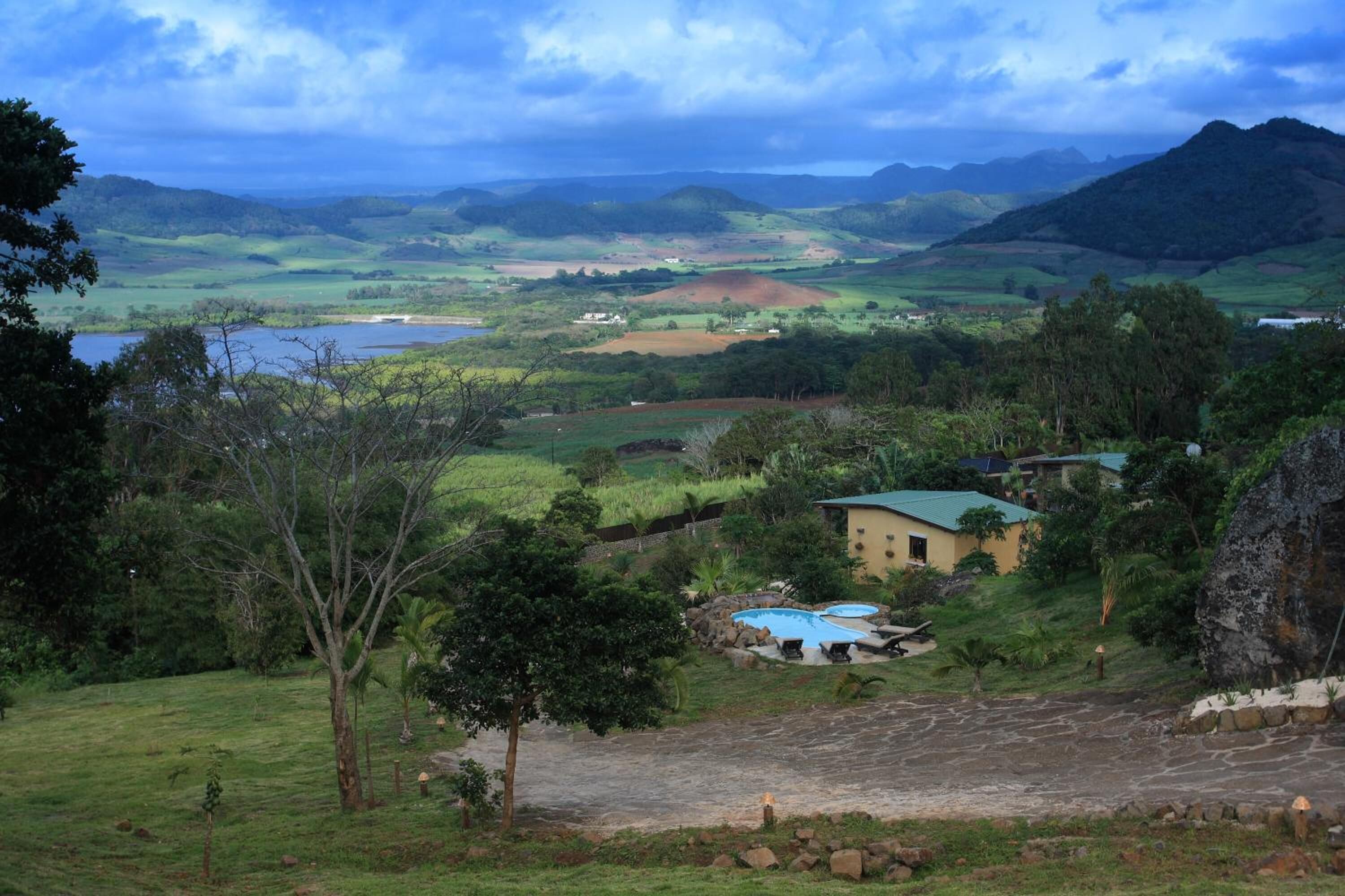 Paisaje rural con una casa, piscina y abundante vegetación.
