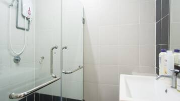 A bathroom with a glass shower enclosure, a white sink, and a handrail.
