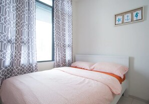 A neatly made bed with a pink and orange bedspread, a white headboard, and a window with patterned curtains. - Centrestage - Heart of Petaling Jaya 2 (Petaling Jaya)