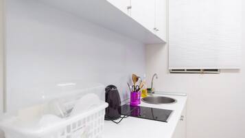 A small kitchenette with white cabinets, a black induction cooktop, a sink, and a window with blinds.