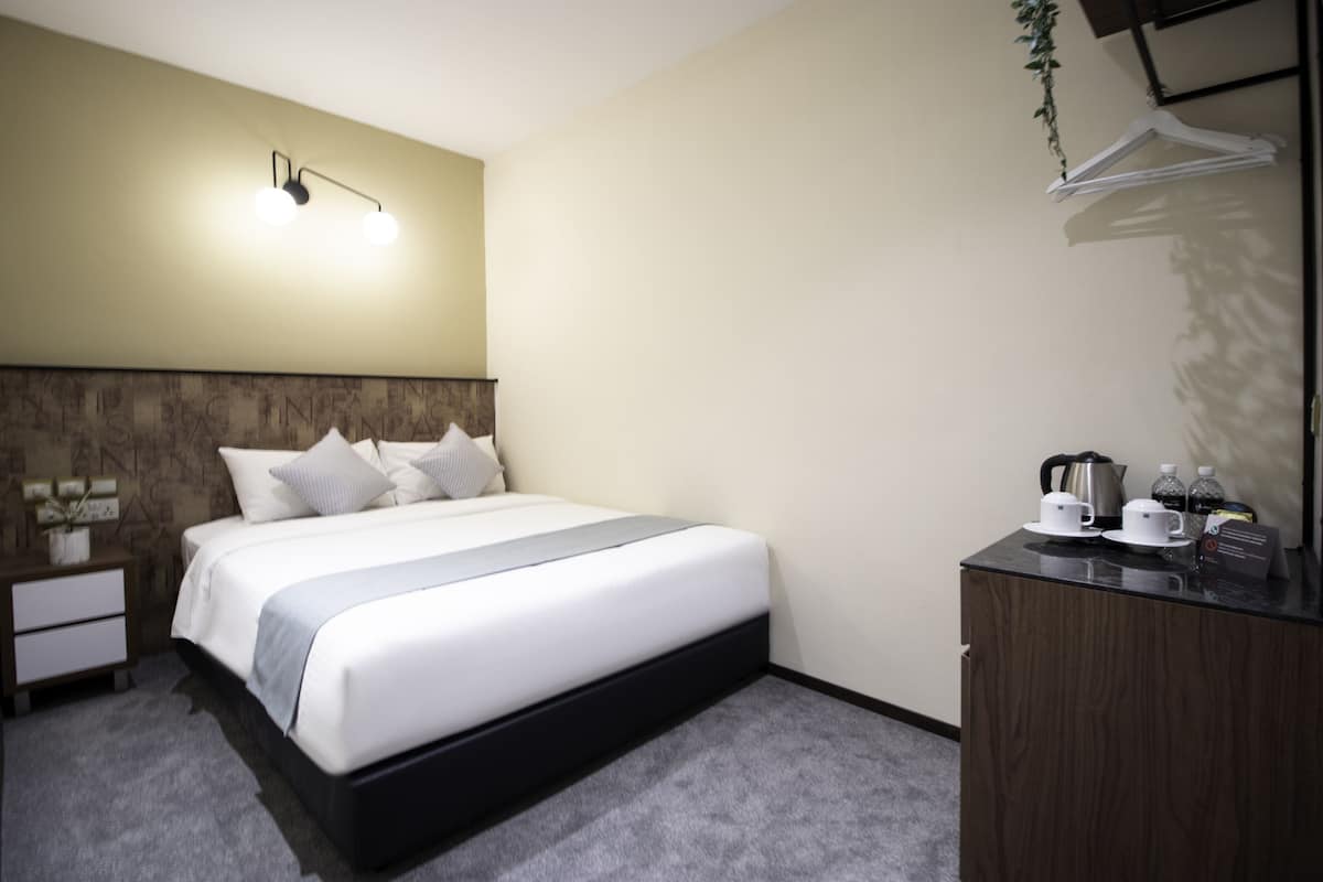 Une chambre d’hôtel comprenant un lit, des tables de chevet, une commode et un luminaire fixé au mur.