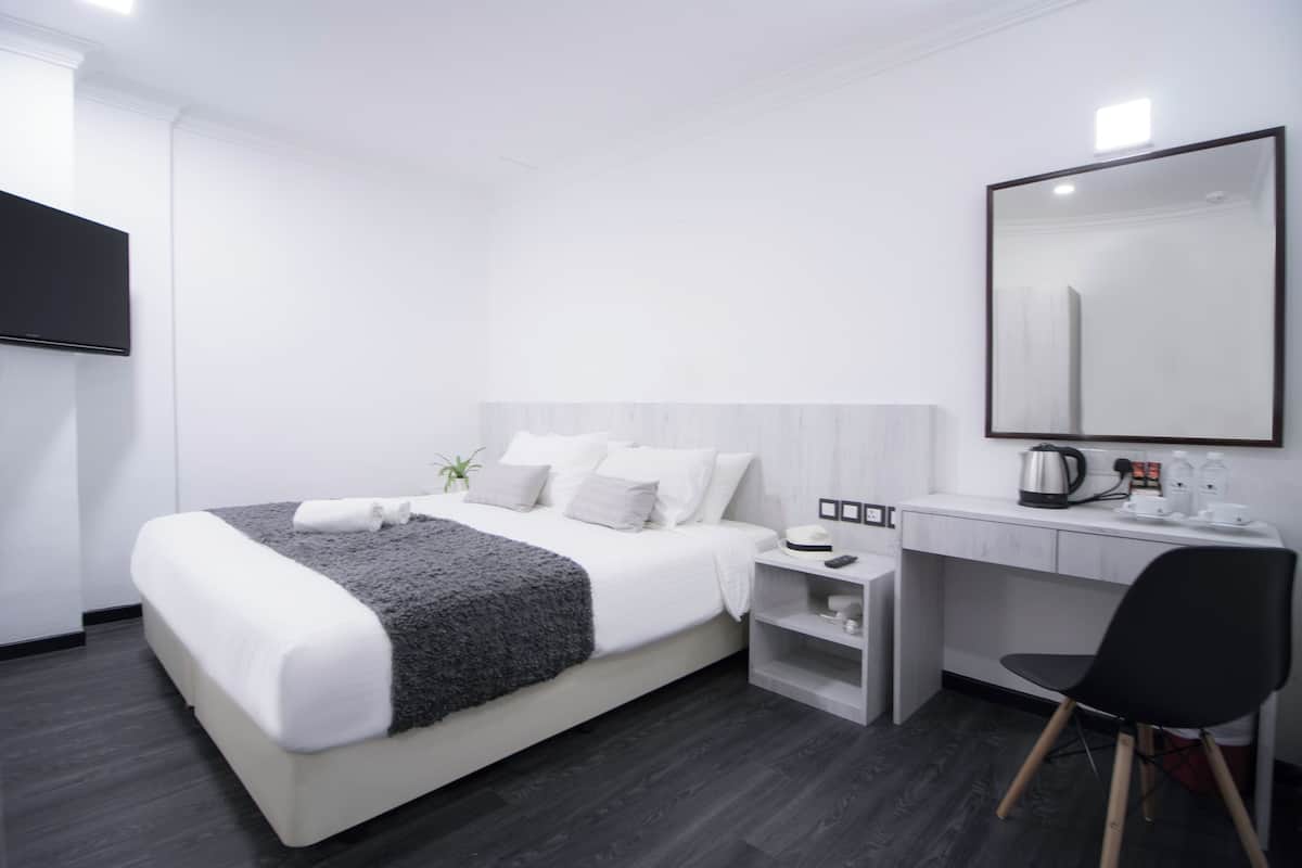 Une chambre d’hôtel moderne avec un lit bien fait, un bureau avec une chaise, un grand miroir et une petite plante.