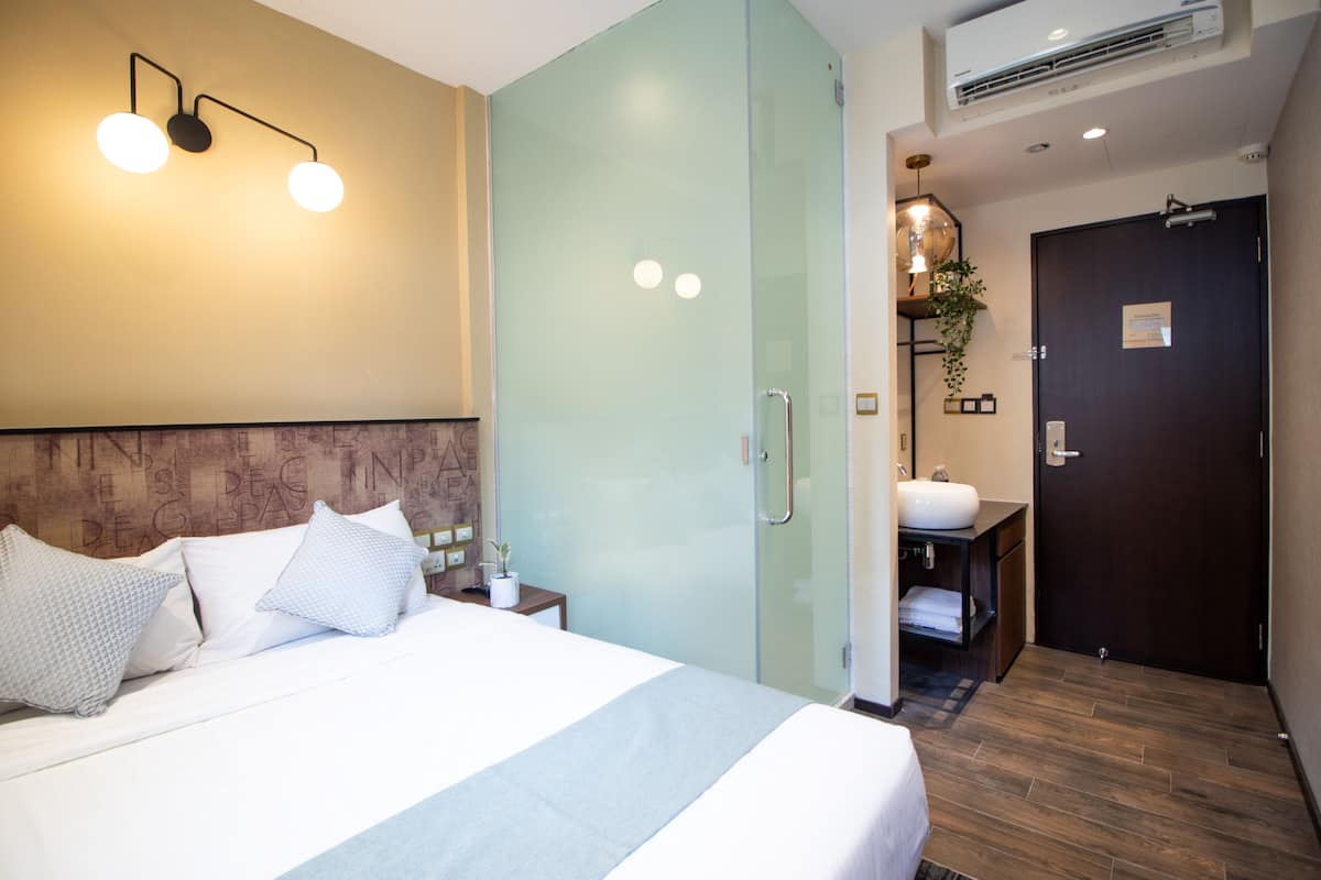 Une chambre d’hôtel comprenant un lit, une table de chevet et une salle de bain avec un lavabo et un miroir.