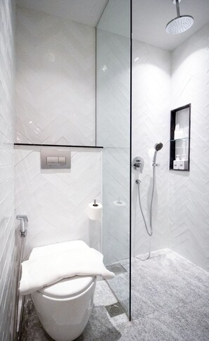 Een moderne badkamer met een glazen douchecabine, een toilet en een klein schapje met toiletartikelen.