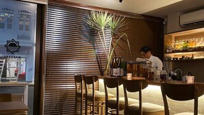 A bar area with wooden slats, a plant, and bar stools. - Harbour Ville Hotel Hamilton - Lavender (Singapore)
