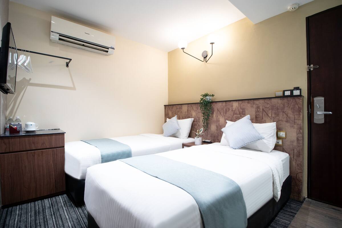 Une chambre d’hôtel avec deux lits, un bureau avec une lampe, un climatiseur et un luminaire fixé au mur.