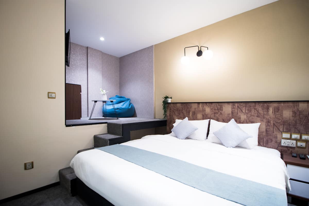 Une chambre d’hôtel moderne avec un grand lit, un bureau sur lequel se trouve un sac bleu et un téléviseur fixé au mur.