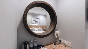 A hotel room with a large round mirror, a bed with white bedding, a hairdryer, and a tray with toiletries. - Harbour Ville Hotel Hamilton - Lavender (Singapore)