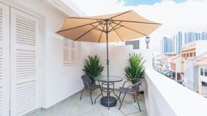 A balcony with a table and chairs, an umbrella, and potted plants. - Harbour Ville Hotel Hamilton - Lavender (Singapore)