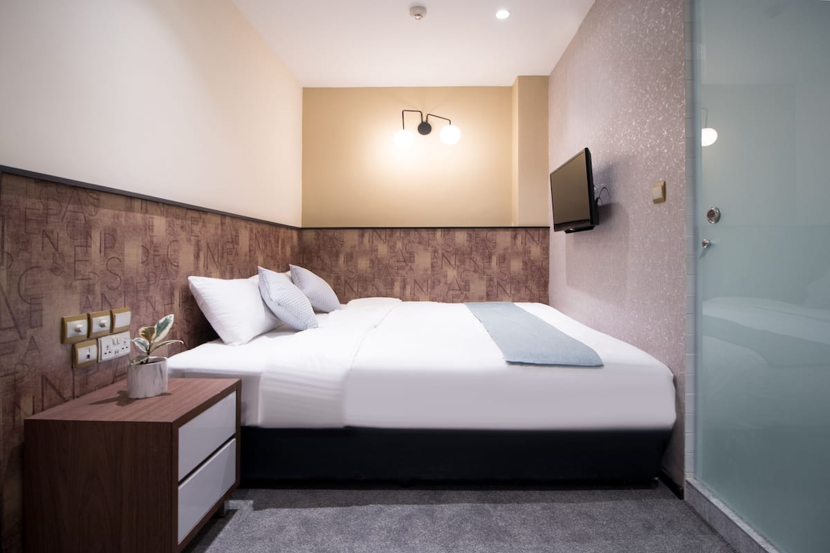 Une chambre d’hôtel moderne avec un lit bien fait, une table de chevet avec une lampe et un téléviseur fixé au mur.