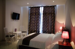 A hotel room with a bed, a desk, a chair, a television, and curtains.