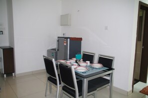 A dining area with a table set for four, chairs, a refrigerator, and a small cabinet.