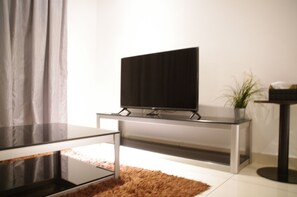 A modern living room with a flat-screen TV on a glass table, a brown rug, and a potted plant.