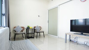 Une chambre moderne et bien éclairée, équipée d’un lit, d’une télévision, d’une petite table avec des chaises et d’une porte-fenêtre coulissante.