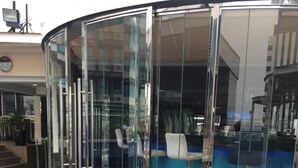 Ein modernes Gebäude mit einem geschwungenen Glaseingang, einer Sitzgelegenheit mit Barhocker und einer Treppe, die zu einer oberen Ebene führt.
