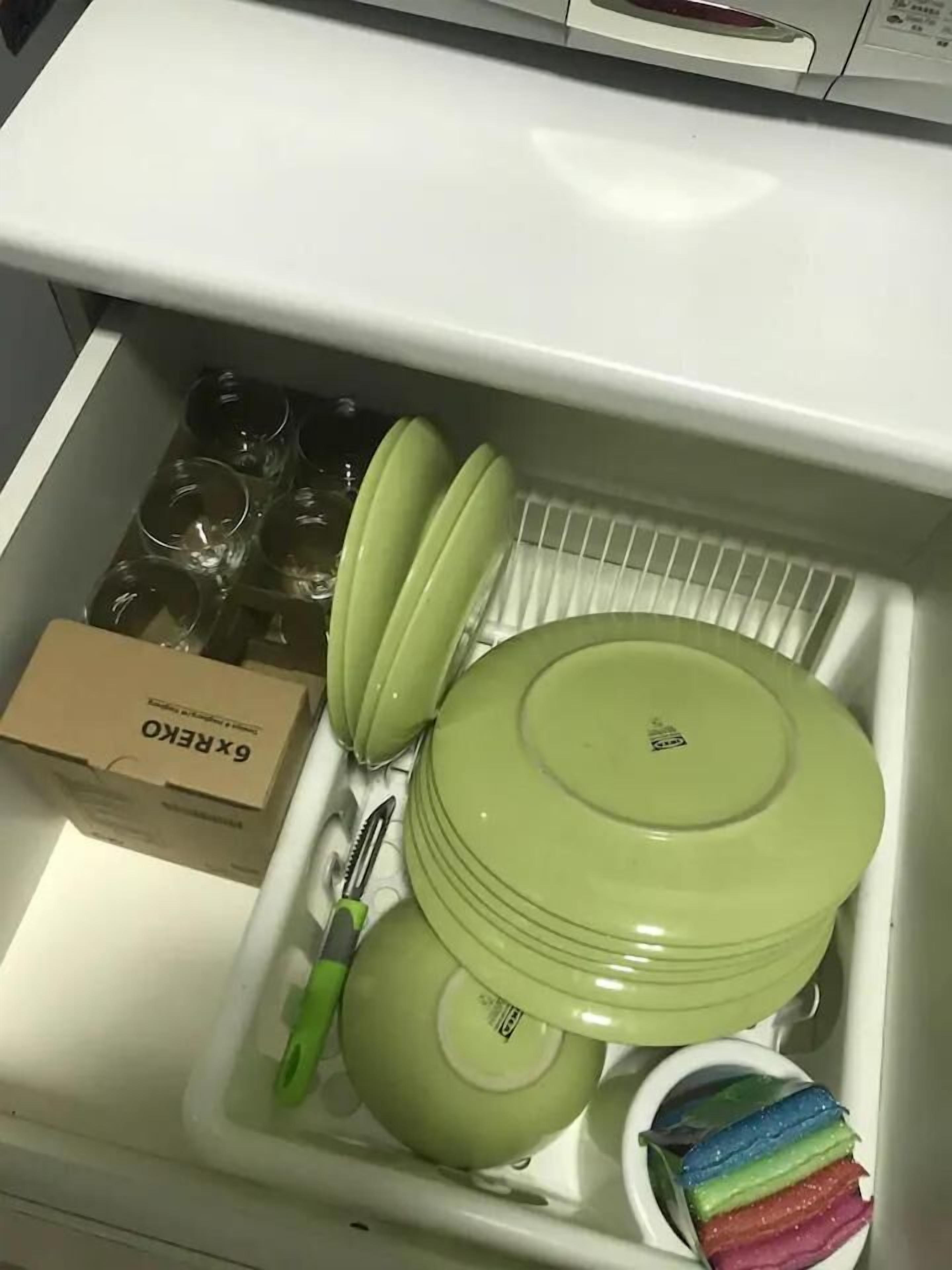Un cajón de cocina con platos verdes, una olla verde, un cuchillo y una caja con la etiqueta 'Gekko'.