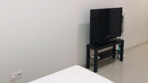 Una habitación con pared blanca, aire acondicionado instalado, televisor de pantalla plana sobre un pedestal negro y una mesa blanca.