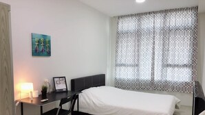 Un dormitorio con cama, escritorio, silla y ventana con cortinas estampadas.