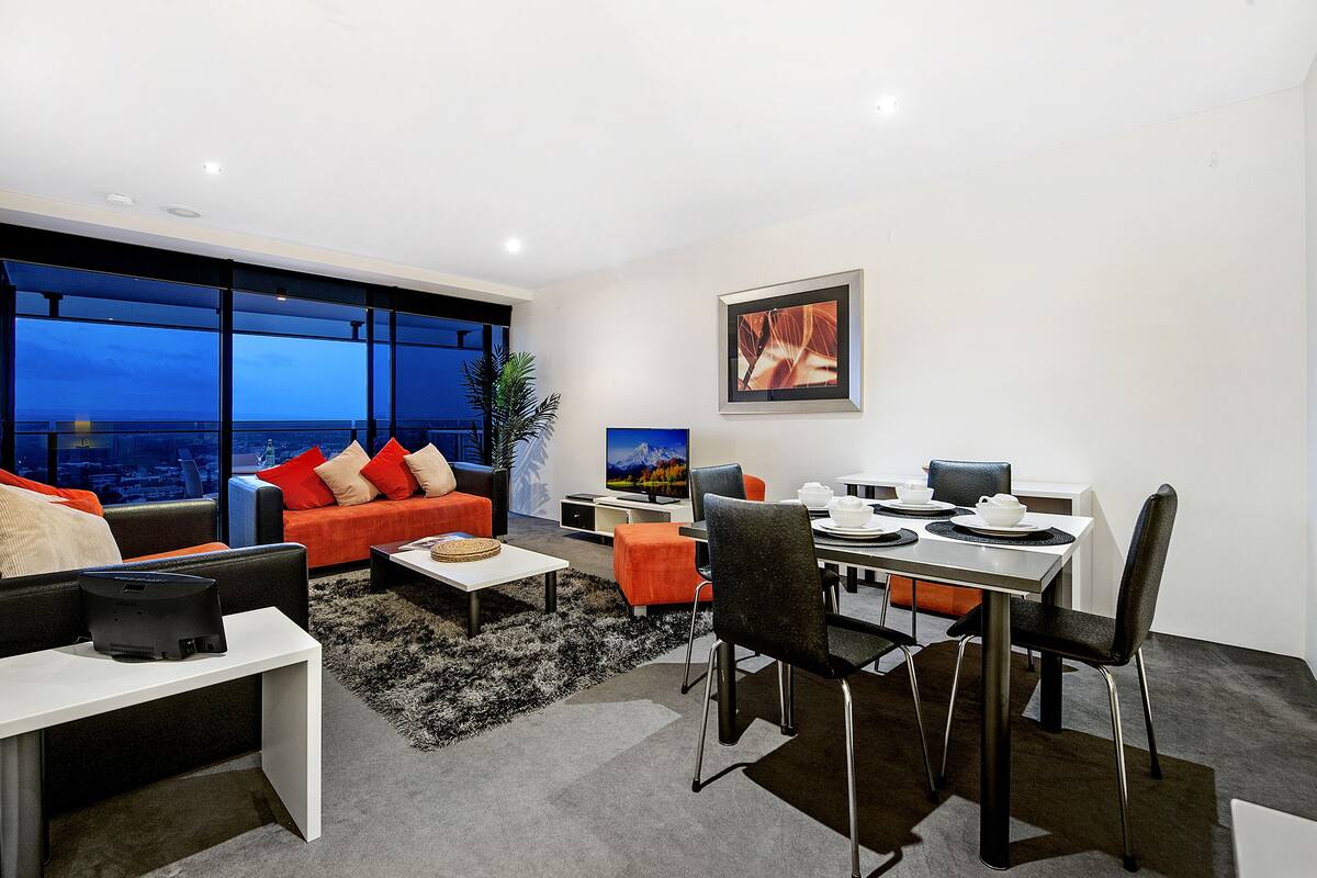 A modern living room with a dining area, large windows with a city view, and contemporary furniture.