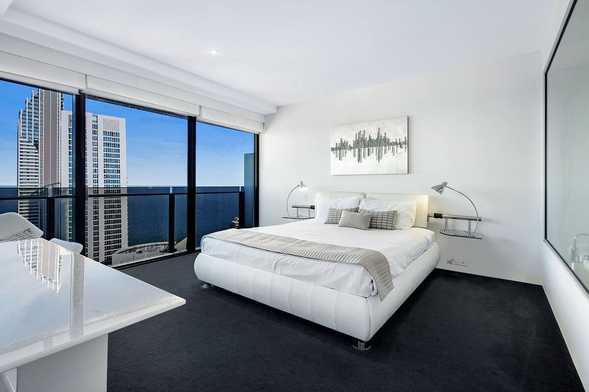 A modern hotel room with a large bed, a desk, and a view of the city skyline.