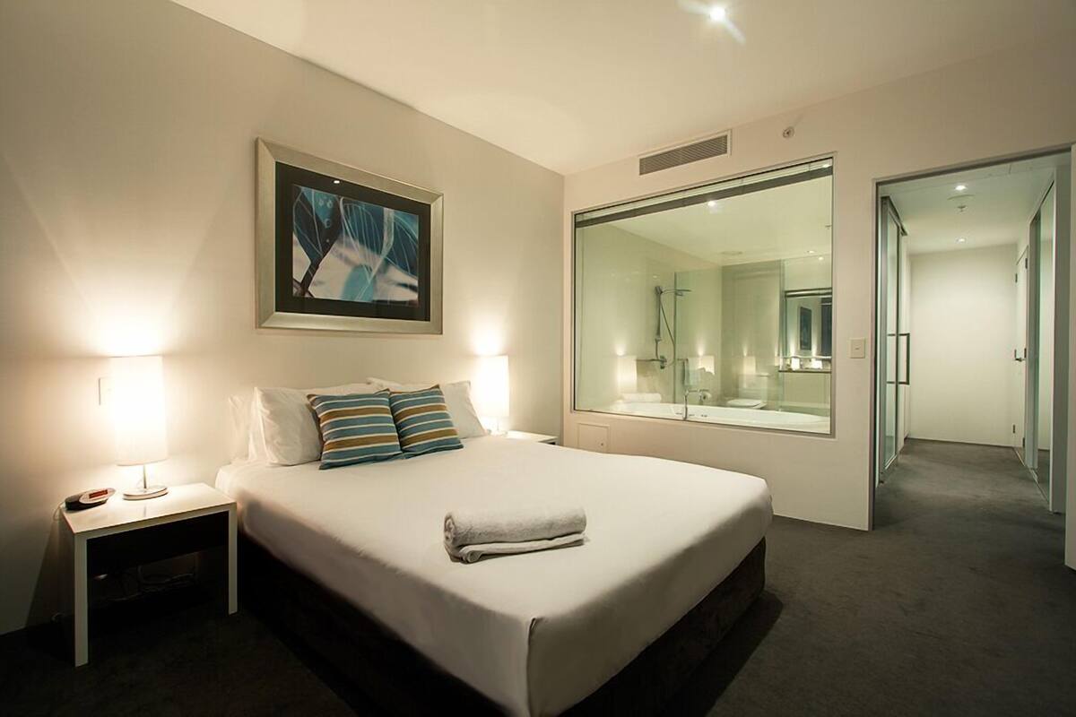 A hotel room with a large bed, bedside lamps, a framed picture, and a large mirror.