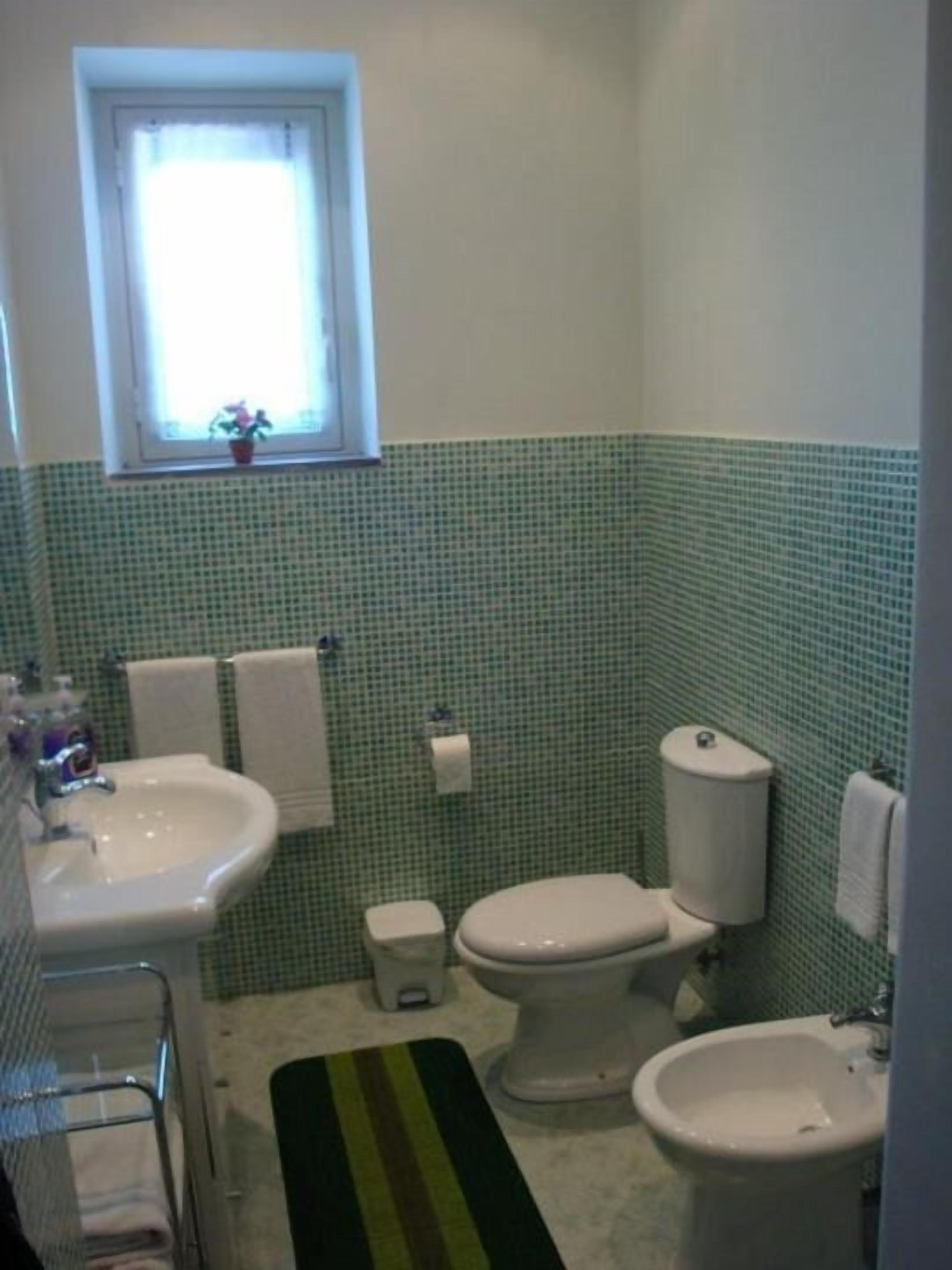 A bathroom with a sink, toilet, bidet, and a small window with a plant.