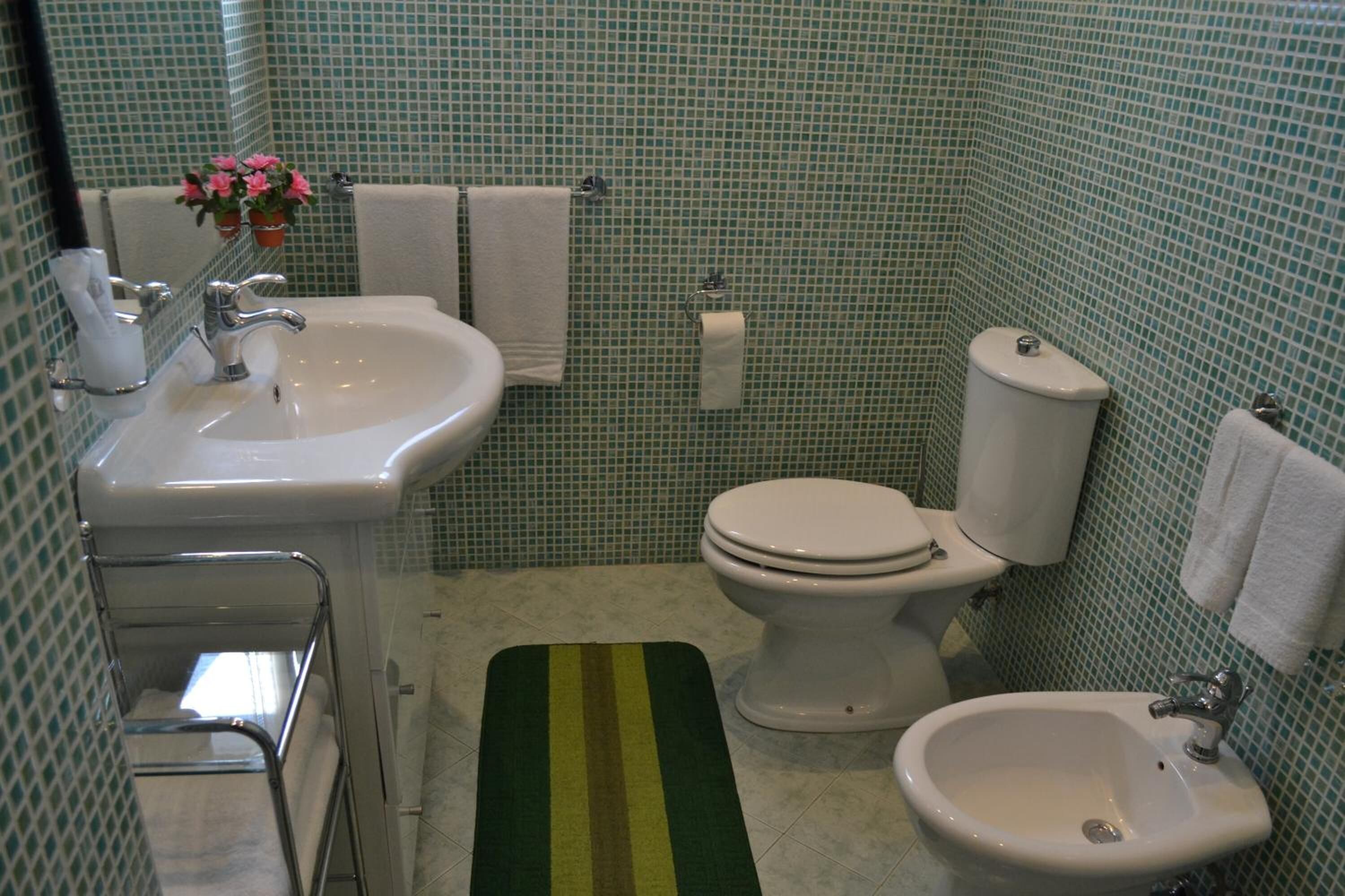 A bathroom with a sink, toilet, bidet, and a green striped rug.
