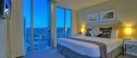 A hotel room with a large bed, a city view, and a flat-screen TV on the wall.