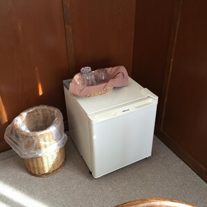 Compact kitchenette with refrigerator, storage baskets, and carpeted floor.