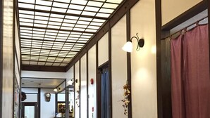 Un pasillo con techo de diseño cuadriculado, luces en la pared, una mesita con lámpara y una puerta al final.