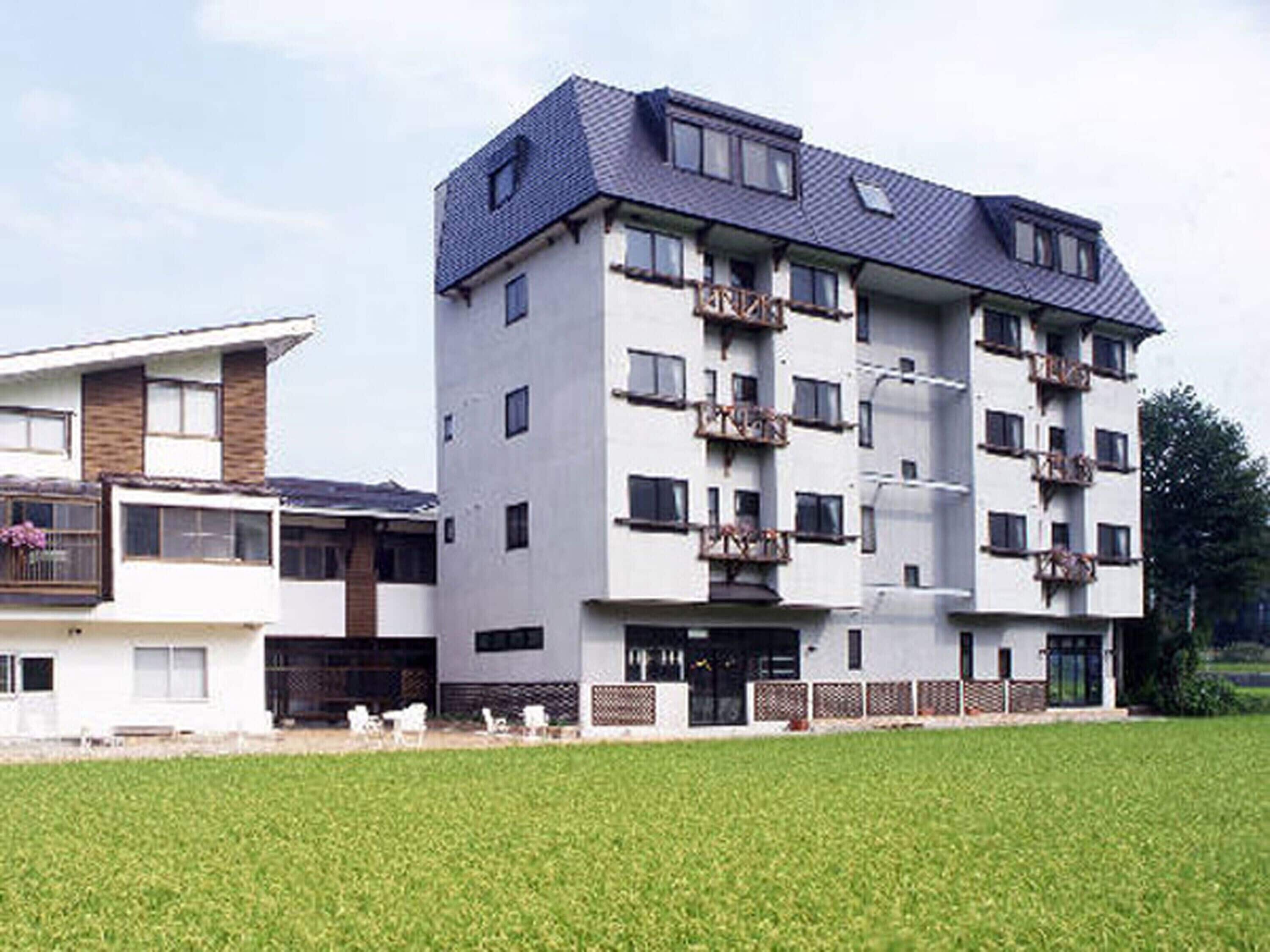 A multi-story residential building with balconies, a flat roof, and a well-maintained lawn in front.