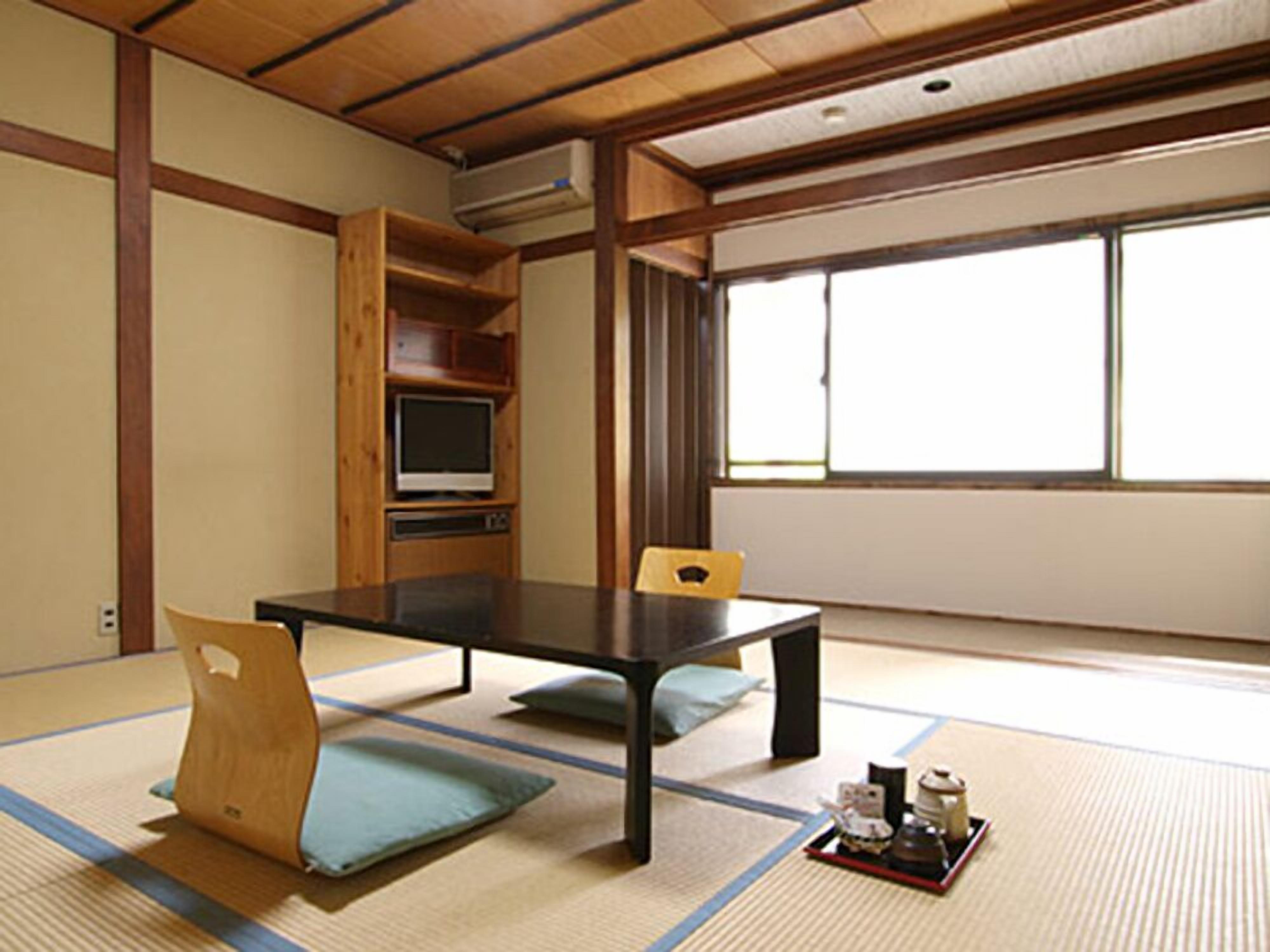 A traditional Japanese room with tatami flooring, a low table, a television, and a window with a view.