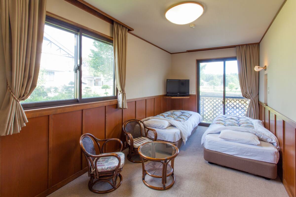A hotel room with two single beds, a television, a small table, and two chairs.