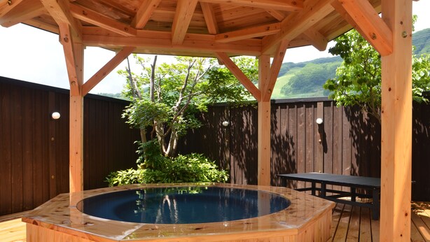 Una bañera de madera bajo una pérgola de madera con vistas a un paisaje verde.