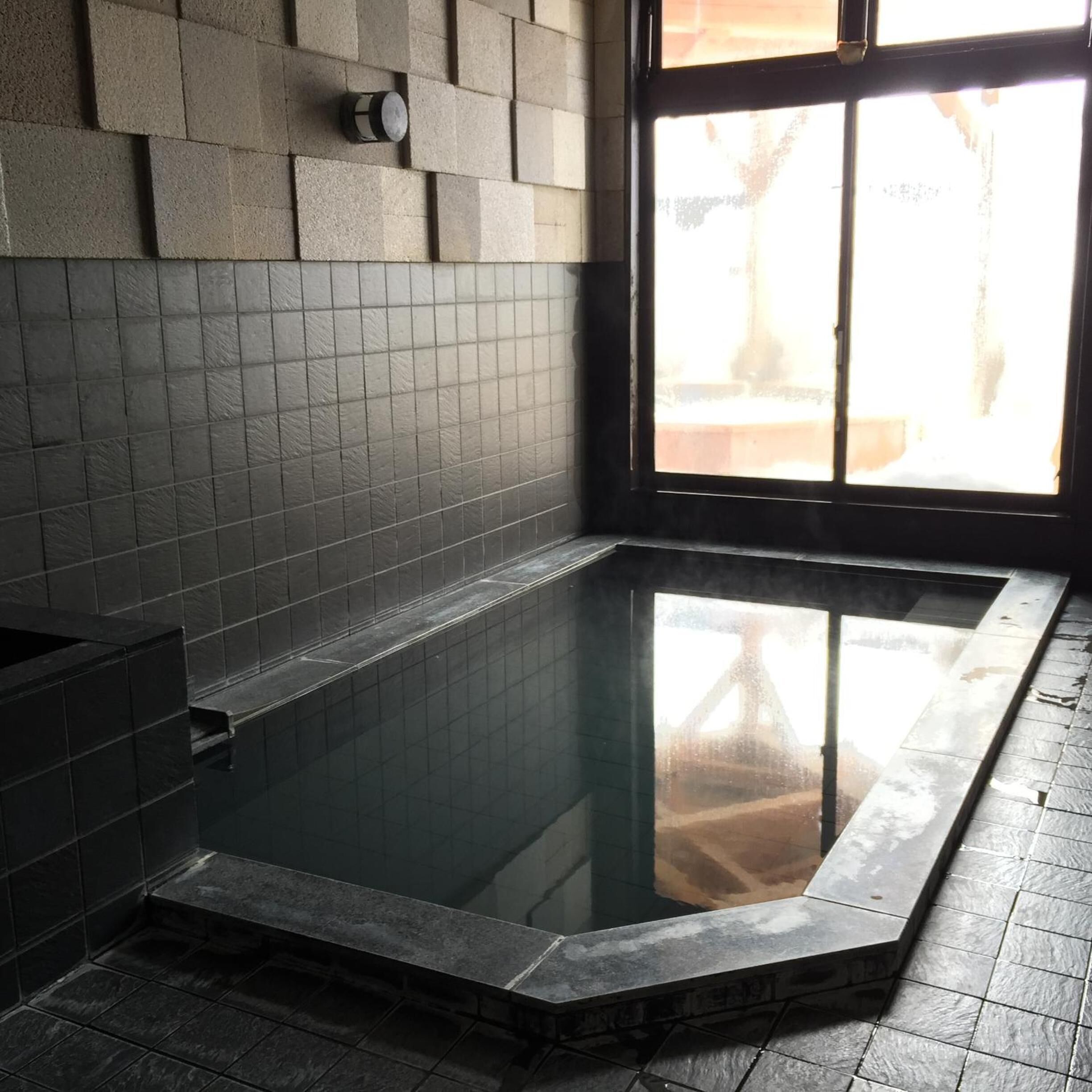 A spa area with a rectangular hot tub, tiled walls, and a window with a view of the outside.